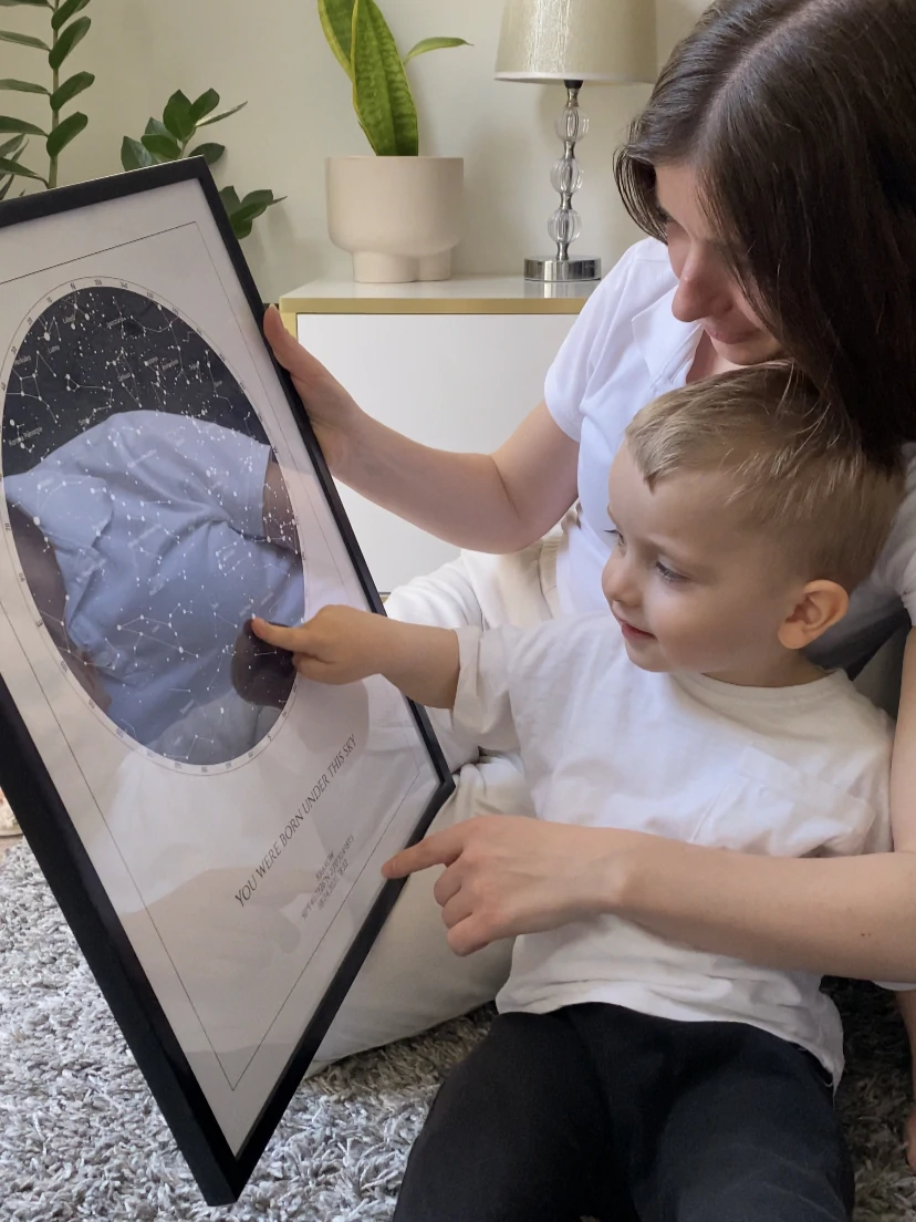 Un băiețel de aproximativ 4 ani se uită cu curiozitate la un tablou cu o hartă a stelelor personalizată.
