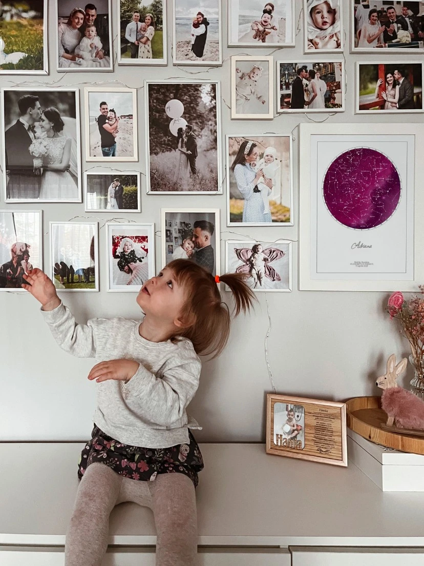 Un tablou cu o hartă a stelelor personalizată pe un fundal roz de cer, prezentat lângă fotografii de familie.
